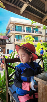 Adorable little girl wearing hat and life jacket sitting in a resort by the beach.