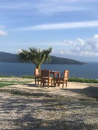 Empty chairs and table by sea against sky