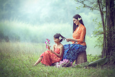 Smiling mother and daughter with flowers sitting on field