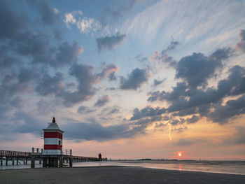 Lighthouse by sea against sky during sunset