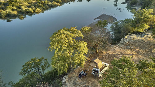 Aerial view of a couple camped with their jeep and rooftop tent and having breakfast in front of the river, cunene river area, angola