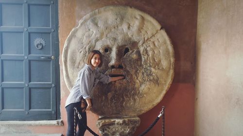 Portrait of woman standing by stone made anthropomorphic face in museum