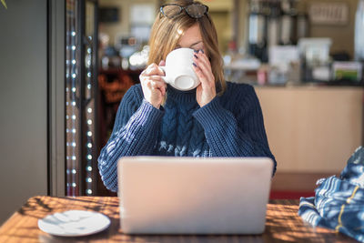 Woman drinking coffee by laptop at table in home