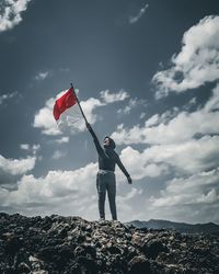 Low angle view of woman holding flag while standing on rock against sky