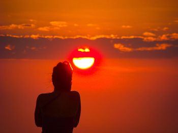 Rear view silhouette of woman standing against sky during sunset