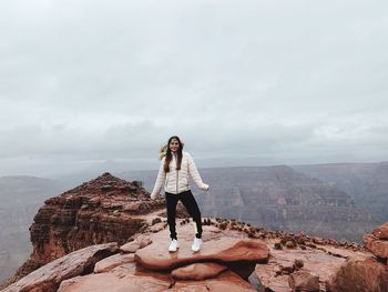 Full length of woman standing on cliff against sky