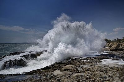 Sea waves splashing on rocks against sky