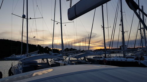 Sailboats moored at harbor against sky during sunset