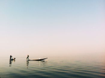 Fishermen in boat on lake against clear sky during sunrise