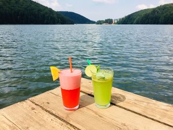 Strawberry lemonade and mint lemonade glasses with straws on wooden pontoon near the lake