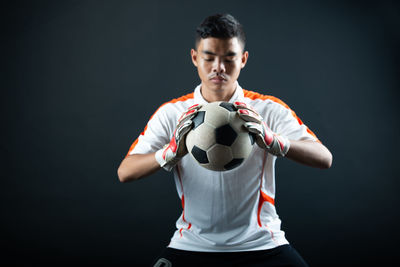 Young man holding ball while standing against black background