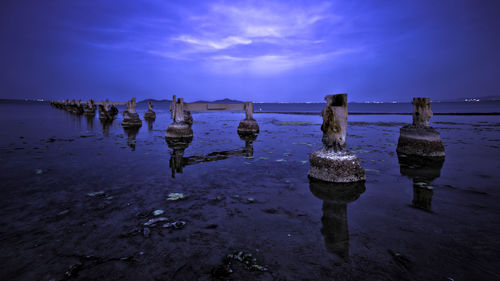 View of wooden posts in sea against sky