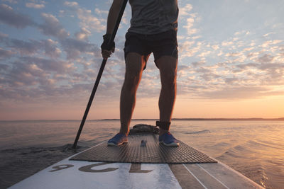 A man is rowing on a stand-up board. far from the coast. sunset sky in background