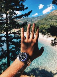 Close-up of man hand wearing wristwatch against trees