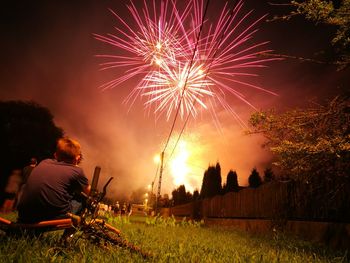 Rear view of boy looking at firework display while sitting on bicycle at night
