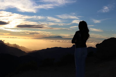 Woman standing on mountain against sky during sunset