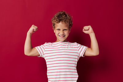 Portrait of boy flexing muscles against red background