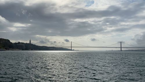 Suspension bridge over sea against cloudy sky