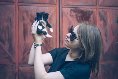 Young woman wearing sunglasses holding kitten in city