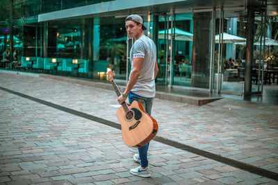 Full length of man playing guitar on footpath