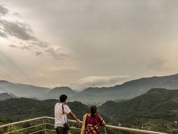 Rear view of mother and son leaning on railing against mountains