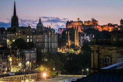 Looking over the streets of edinburgh towards an illumined edinburgh castle.