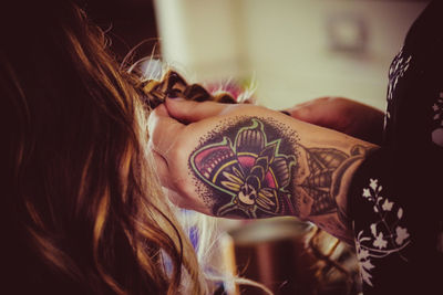 Cropped image of woman with tattooed hand braiding hair