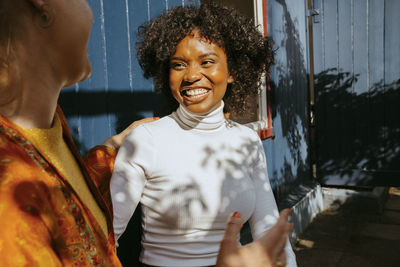 Happy young woman in turtleneck talking with female friend at dinner party