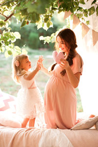 Pregnant mother holding heart shape playing with daughter