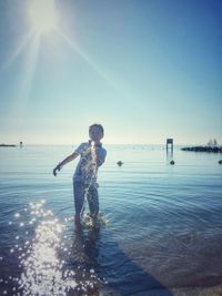 Portrait of boy splashing water while standing in sea against sky