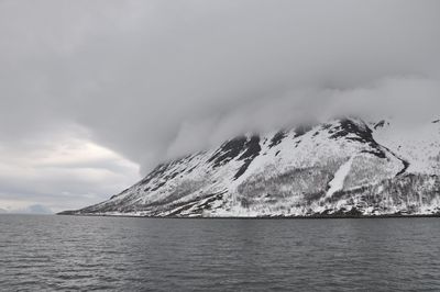 Scenic view of sea by snowcapped mountain against sky