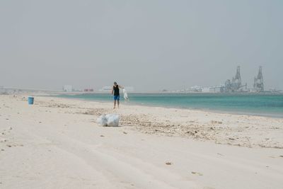 Man doing beach clean up overlooking big factory