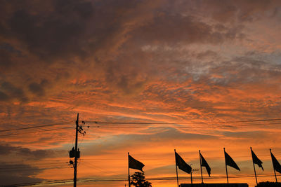 Low angle view of silhouette cranes against dramatic sky during sunset