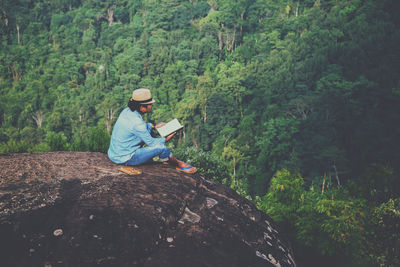 High angle view of man wearing hat sitting on cliff