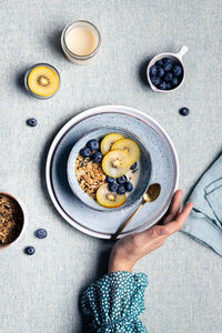 Top view of crop anonymous female with breakfast with bowl with granola and blueberries and kiwi slices