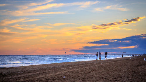 Silhouette people standing on beach against sky during sunset