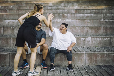 Young woman giving high-five to woman sitting with male friend on steps