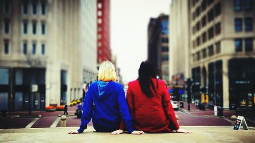 Rear view of friends sitting on retaining wall looking at city