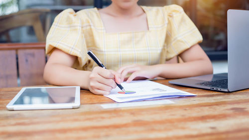 Midsection of woman using mobile phone while sitting on table