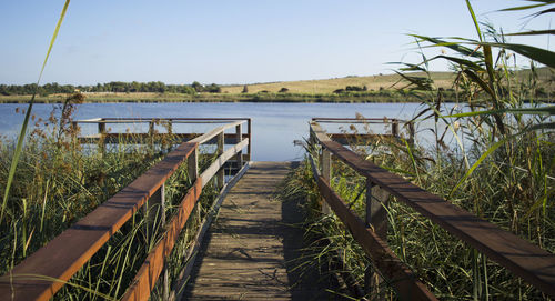 Wooden railing by lake against sky