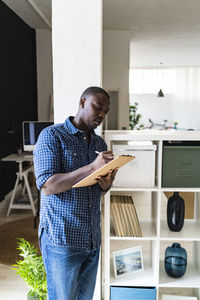 Man writing while holding clipboard at home