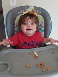 High angle view of cute boy sitting in high chair at home acting silly balancing bread on head