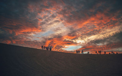 Silhouette of people on sand dune during sunset