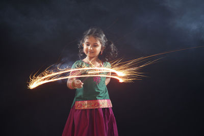 Girl spinning sparkler while standing against black background