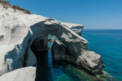 Rock formation in sea against clear blue sky