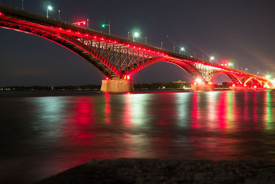 Illuminated bridge over river against sky at night