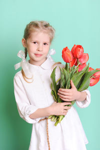 Portrait of cute girl holding yellow flowers against blue background