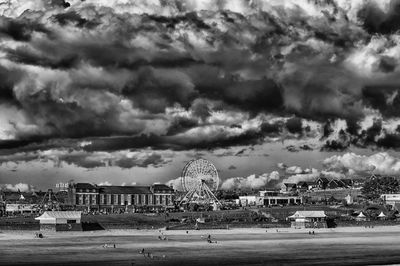 Ferris wheel at beach against cloudy sky