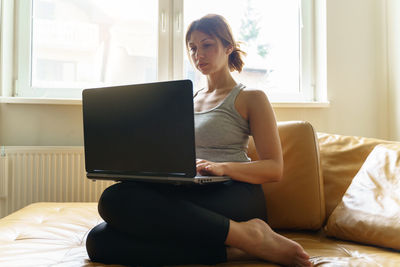 Young woman using phone while sitting on bed at home