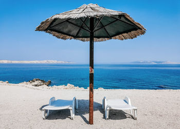 Empty deck chairs under straw parasol on beach on sunny day in summer.